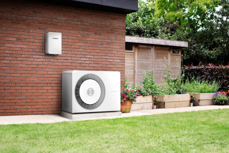 Das Bild zeigt Garten eines Einfamilienhauses mit einer Wärmepumpe vorm Haus.